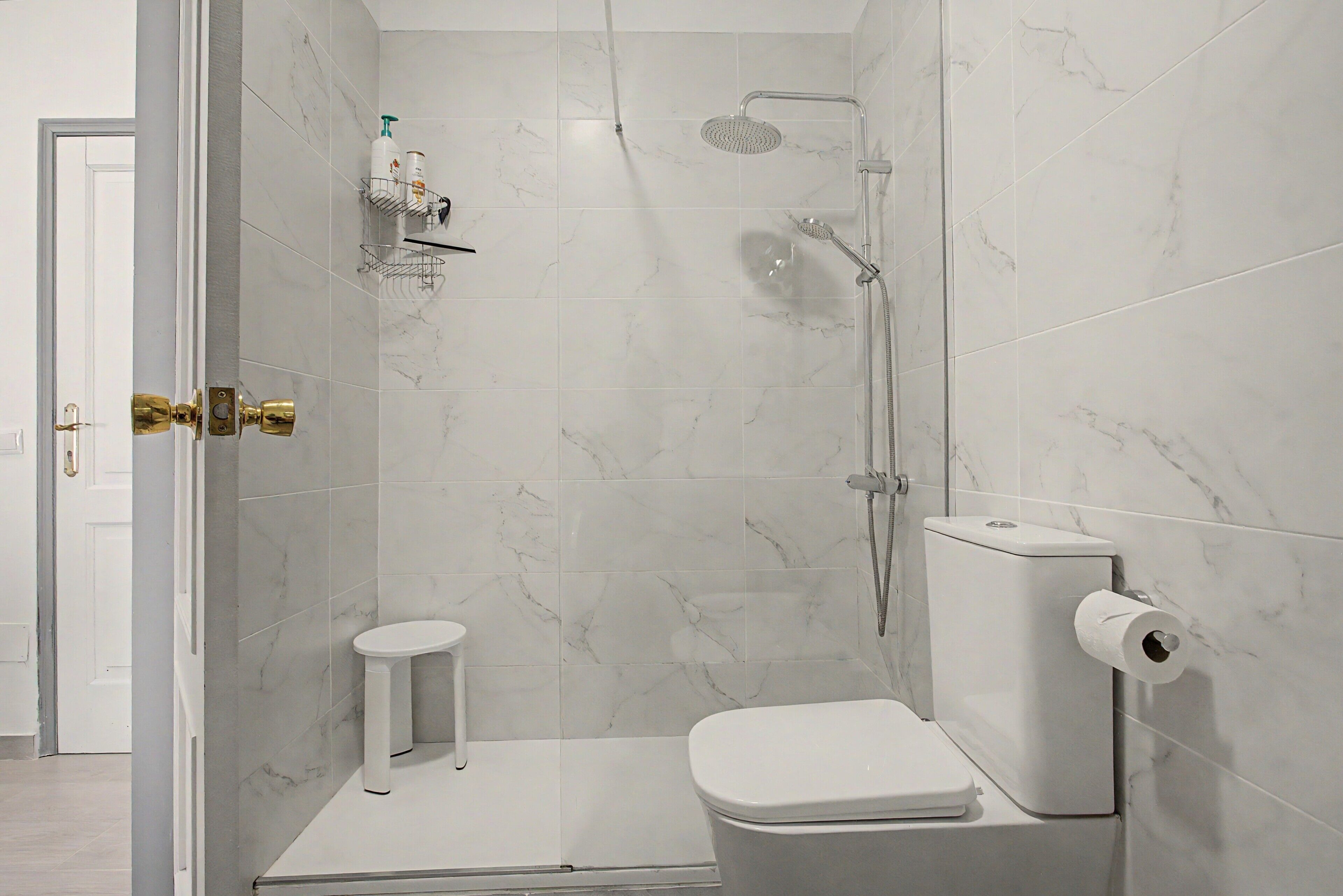Un baño pequeño con ducha, inodoro y un taburete.