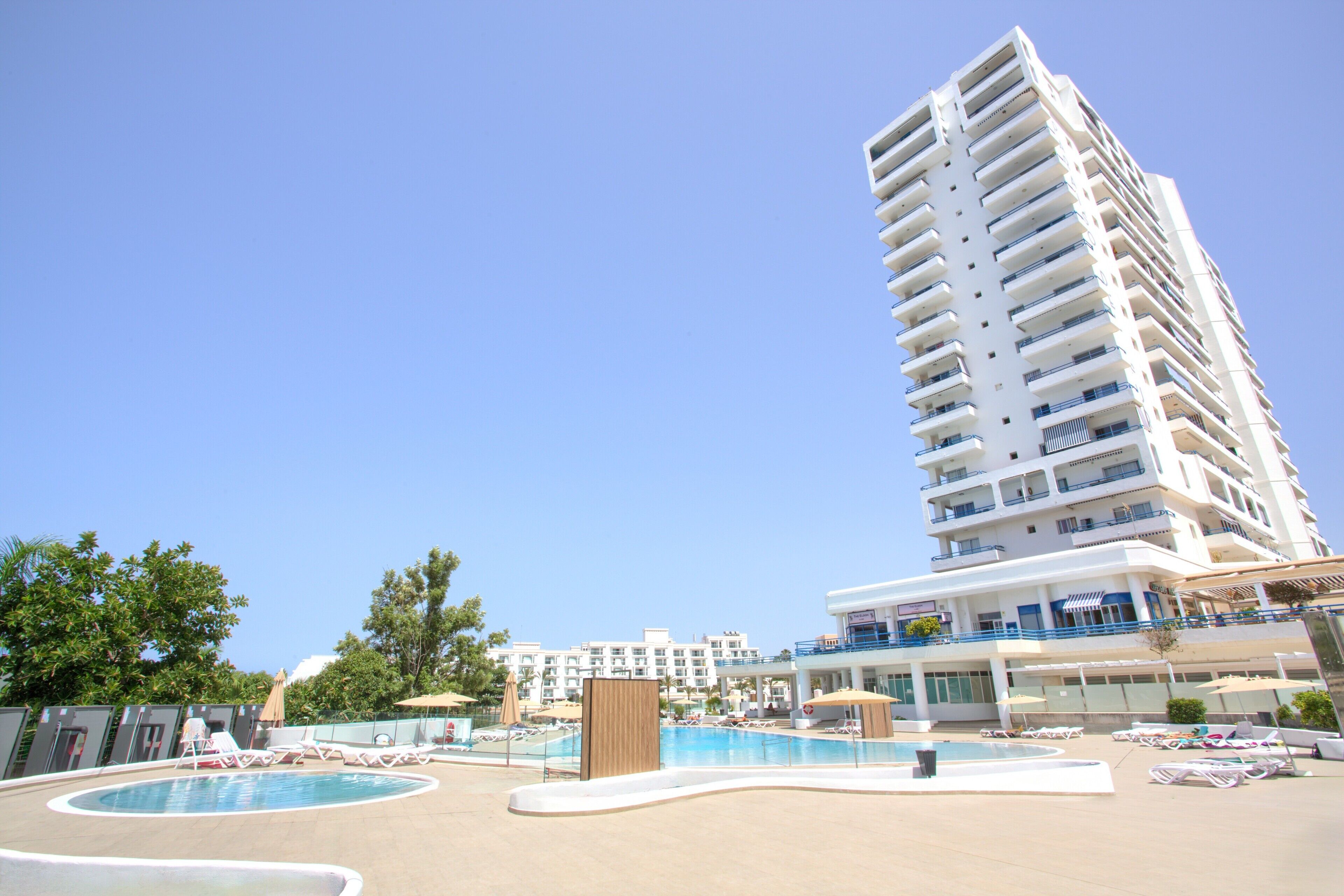 Un hotel de gran altura con área de piscina, varios balcones y cielo despejado.