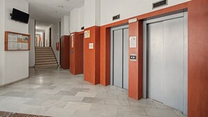 Un pasillo con varios ascensores, una escalera y un tablón de anuncios.