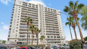 Un hotel de varios pisos con balcones, palmeras y un cielo despejado.