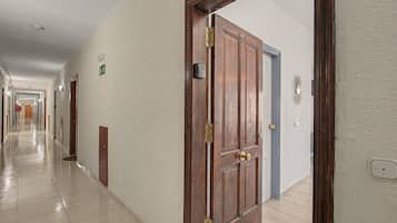 A hotel corridor with wooden doors, a hallway with a tiled floor, and a wall-mounted emergency exit sign.