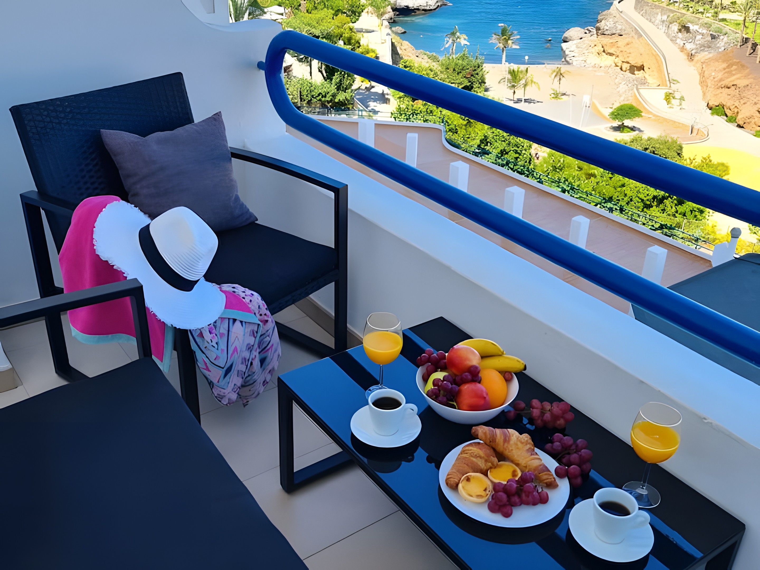 Un balcón con una mesa dispuesta para el desayuno, incluyendo cruasanes, fruta y bebidas.