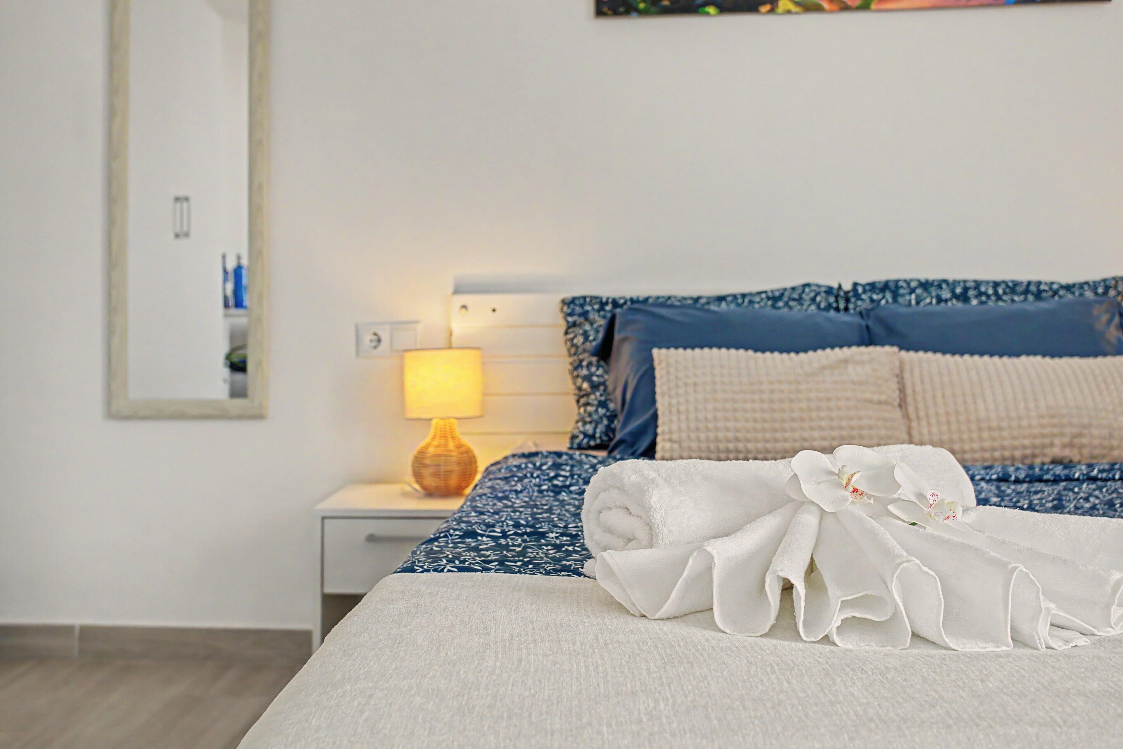 Una cama bien hecha con una toalla blanca y otra toalla blanca enrollada, sobre ropa de cama azul estampada.