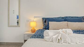 Una cama bien hecha con una toalla blanca y otra toalla blanca enrollada, sobre ropa de cama azul estampada.