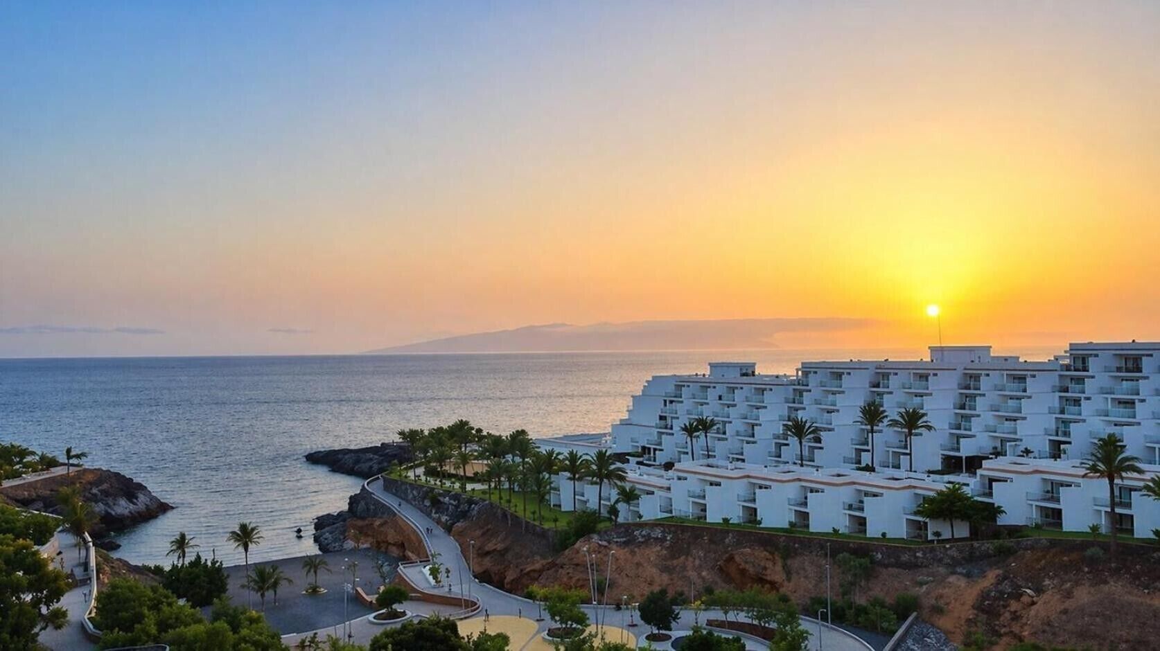 Un hotel frente al mar con vistas al océano, edificios blancos y palmeras.