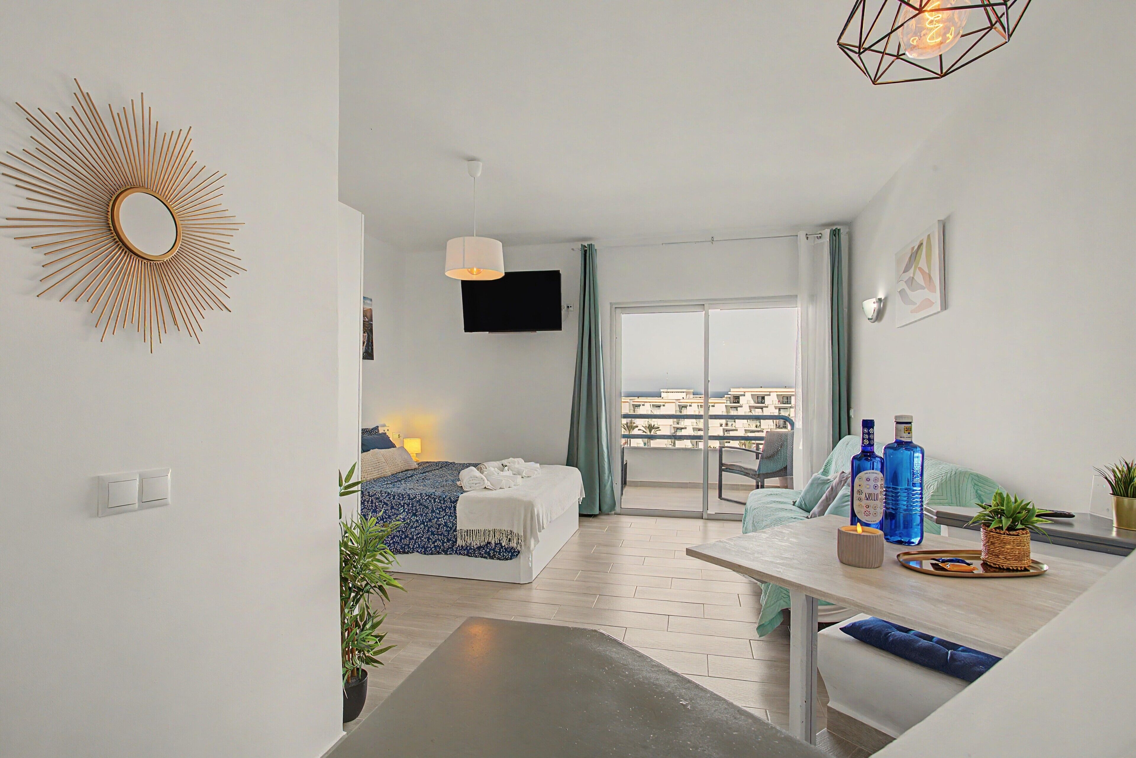Habitación de hotel moderna con cama, escritorio, televisión de pantalla plana, balcón con vistas y decoración mural con diseño de sol.