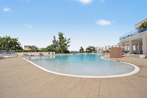 Ein Swimmingpool mit Liegestühlen und Sonnenschirmen, umgeben von viel Grün und Gebäuden.