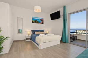 A modern bedroom with a bed, bedside tables, a painting, and a view of the sea. - Dream Ocean Sunset Apartment with Sea Views, Shared Garden, and Wi-Fi (Adeje)