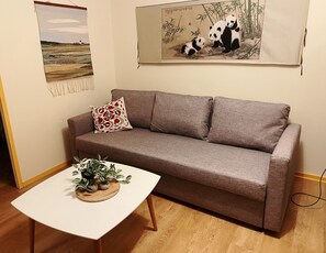 Ein Wohnzimmer mit einem braunen Sofa, einem weißen Tisch mit Pflanzen und zwei Wandbildern.