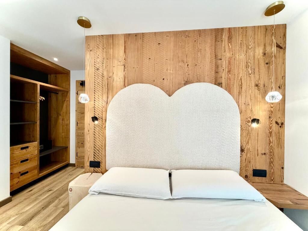 A bedroom with a wooden headboard, a bed with white linens, and a built-in wardrobe.