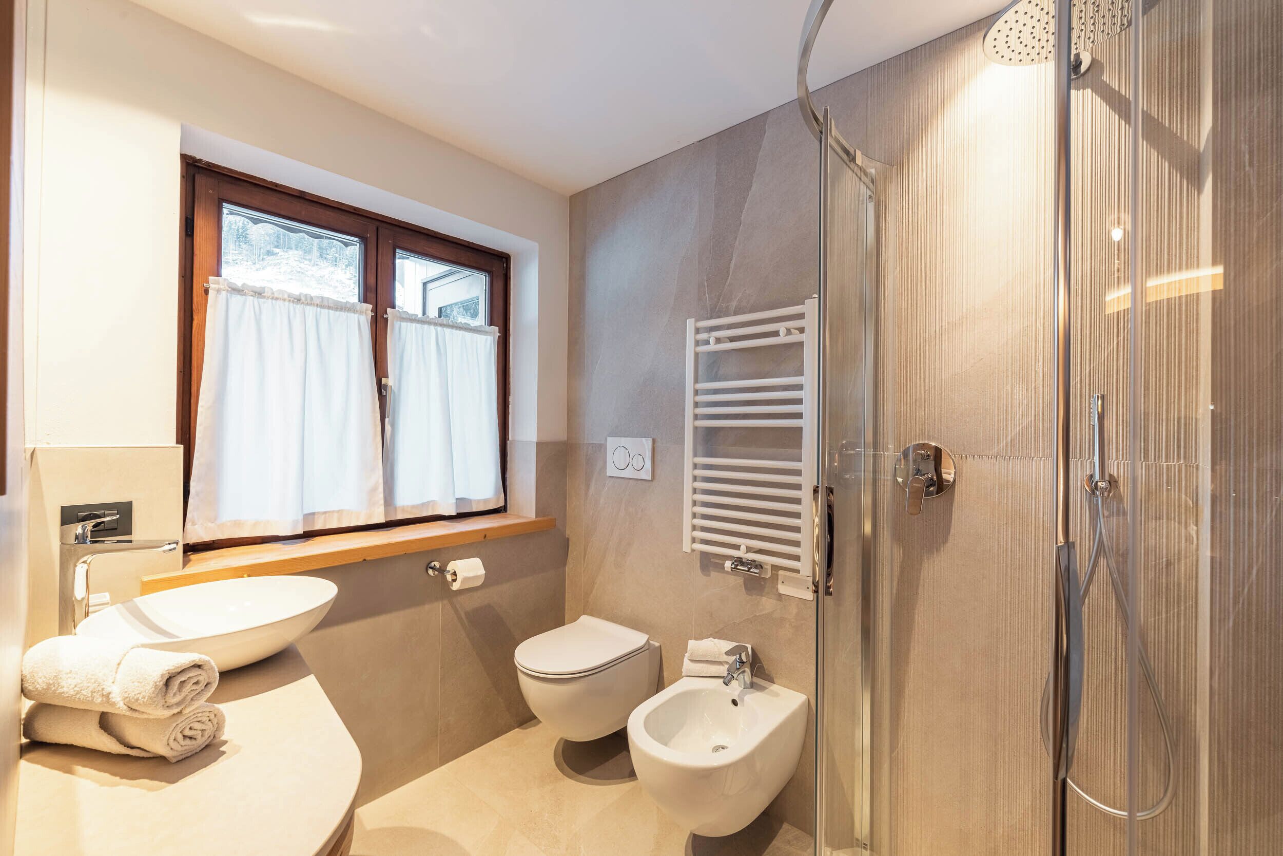 A modern bathroom with a sink, toilet, bidet, and a glass-enclosed shower.