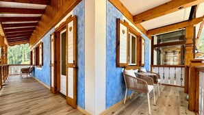 A covered corridor with wooden beams, a dining area with chairs, and a view of the outdoors. - Cesa Planber Apartments Mountain View (Canazei)