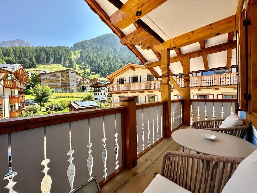 Un balcón con vistas a un paisaje montañoso, barandas de madera y una mesa con sillas.