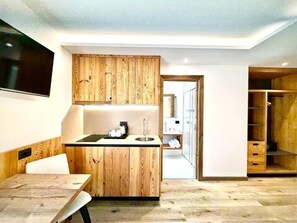A modern kitchen with wooden cabinetry, a built-in sink, and a dining area with a bench. - Cesa Planber Apartments Mountain View (Canazei)
