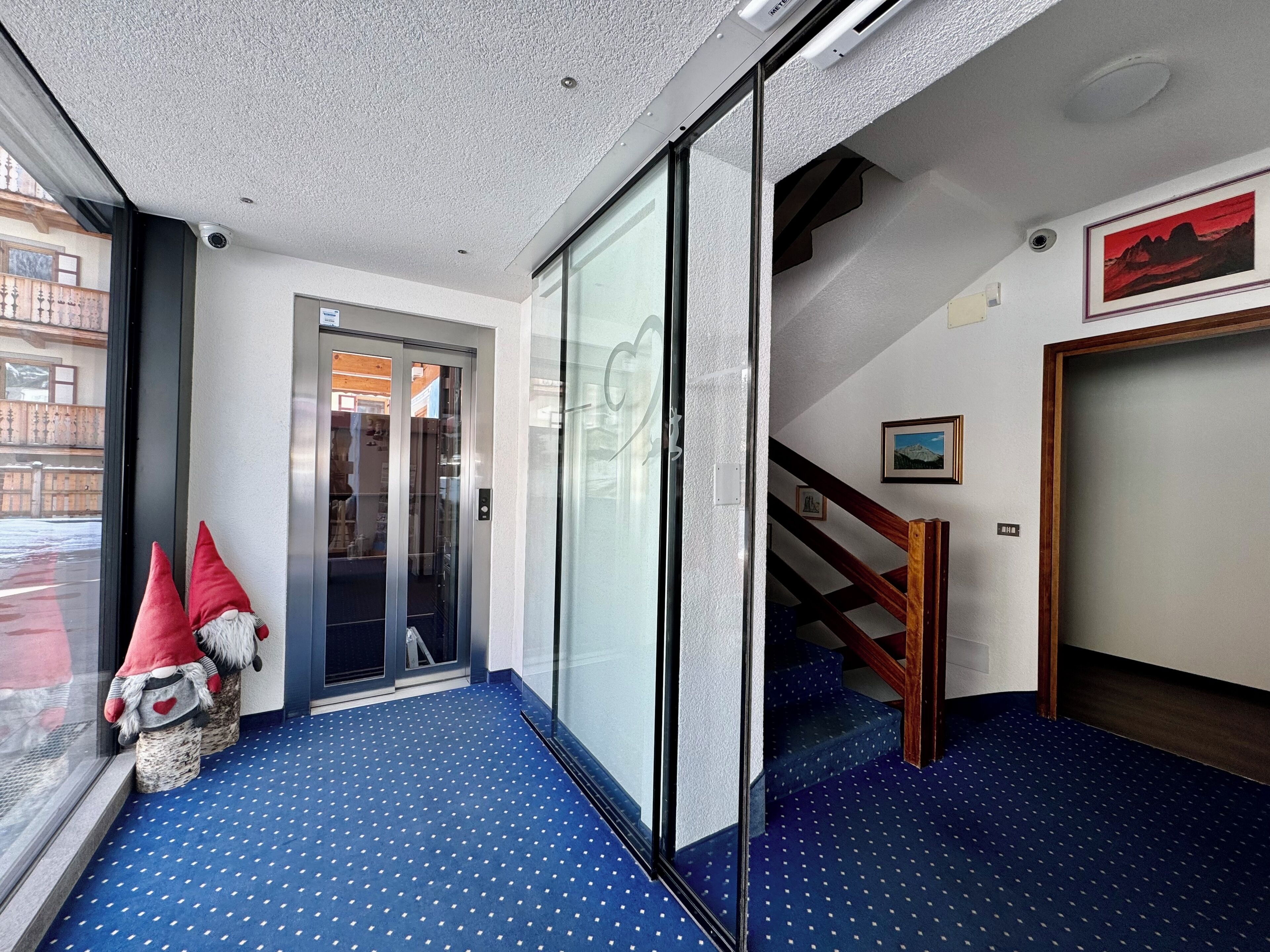 A hotel lobby with a blue carpet, a glass door entrance, a staircase, and a framed picture on the wall.