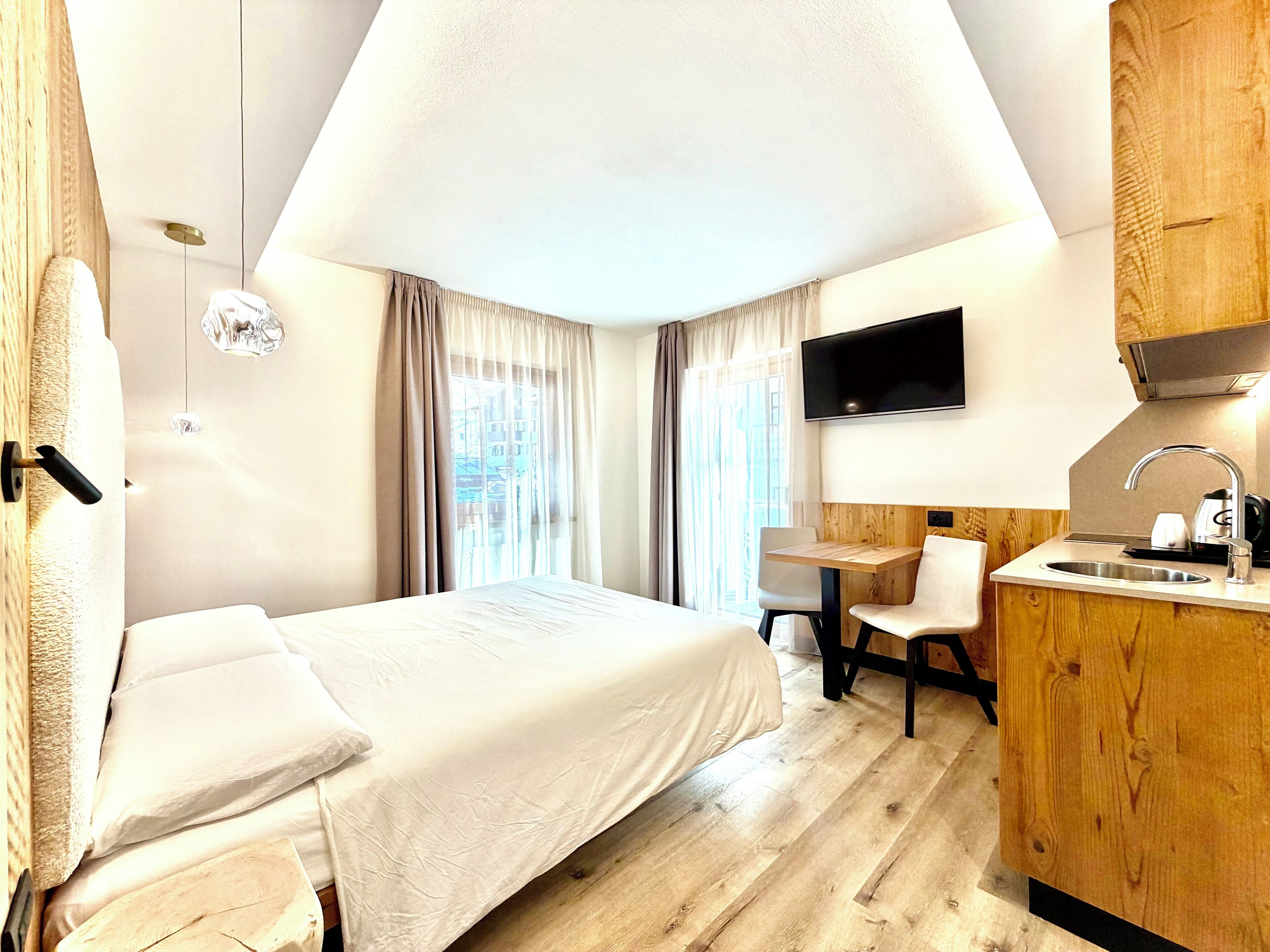 A hotel room with a bed, a desk, a chair, a TV, and a kitchenette.