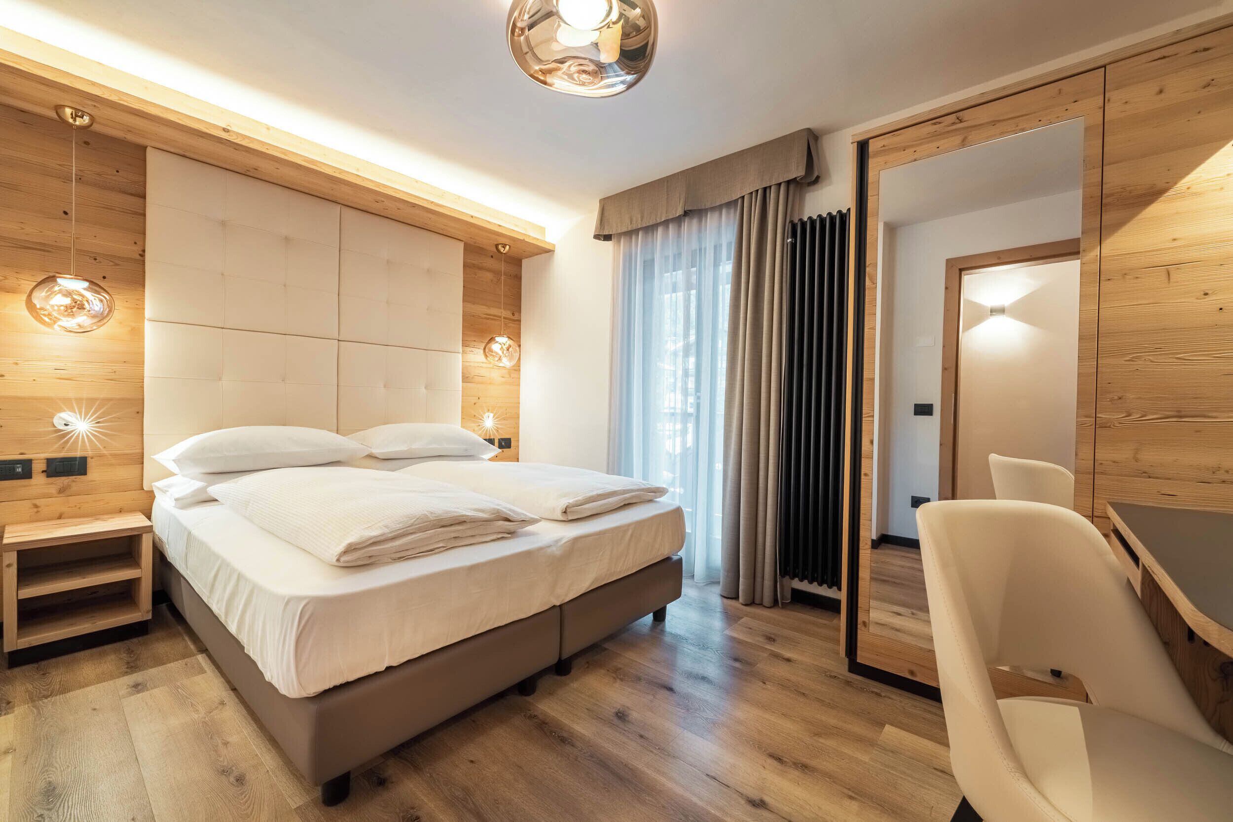 A modern bedroom with a large bed, bedside tables, a desk, and a mirror.