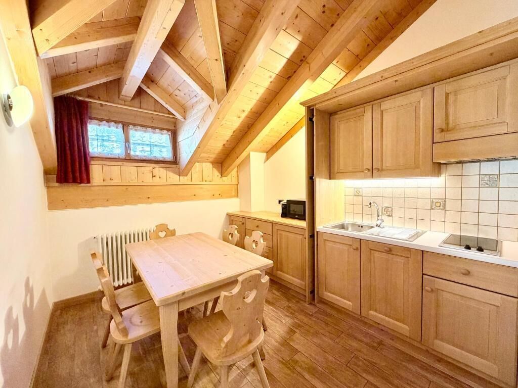 A kitchen with wooden cabinets, a white countertop, and a window with a red curtain.