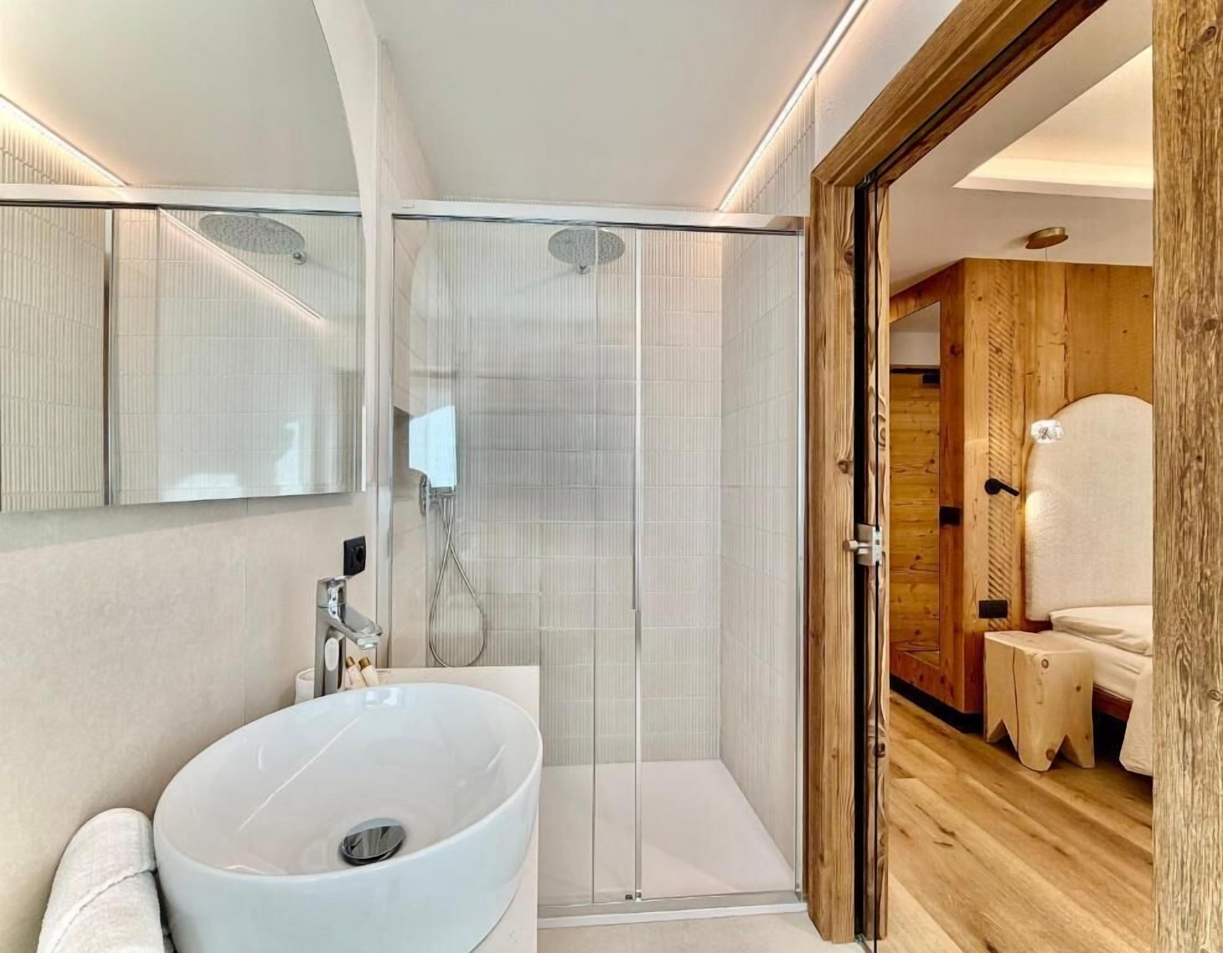 Een moderne badkamer met een grote witte wastafel, een douche met glazen wanden en houten details.