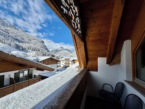 A wooden balcony with a view of snow-covered buildings and mountains.