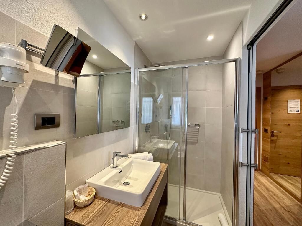 A modern bathroom with a glass shower enclosure, a white sink, and a wooden vanity.