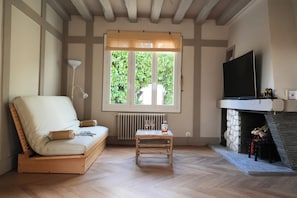 A room with a sofa, a small table, a fireplace, a TV, and a window with a view of greenery. - Gîte Premium Japonais 4★ - Clim & Borne VE - 4 min du Zoo de Beauval (Saint-Aignan)