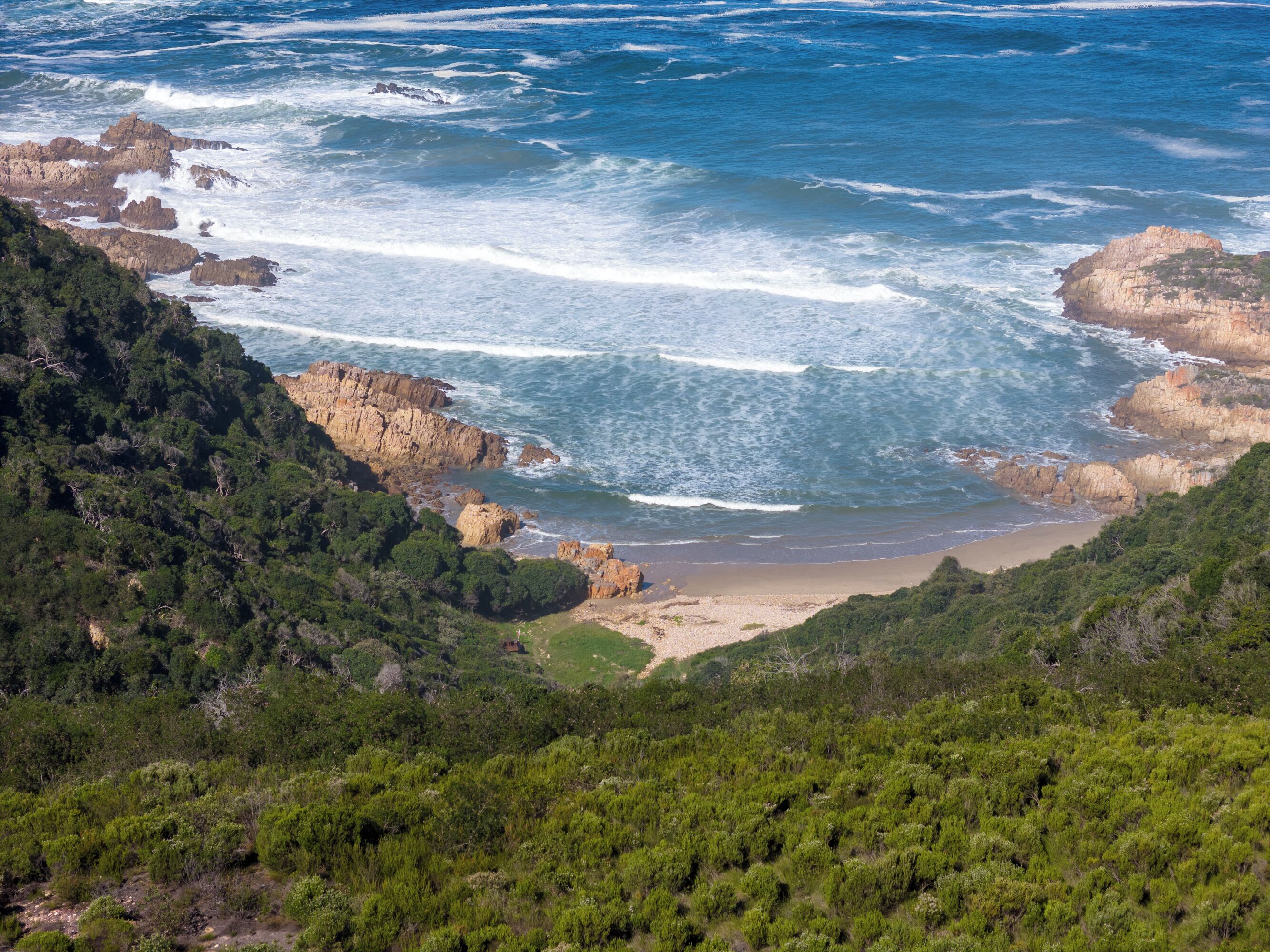 A coastal landscape with rocky cliffs, a beach, and dense greenery.