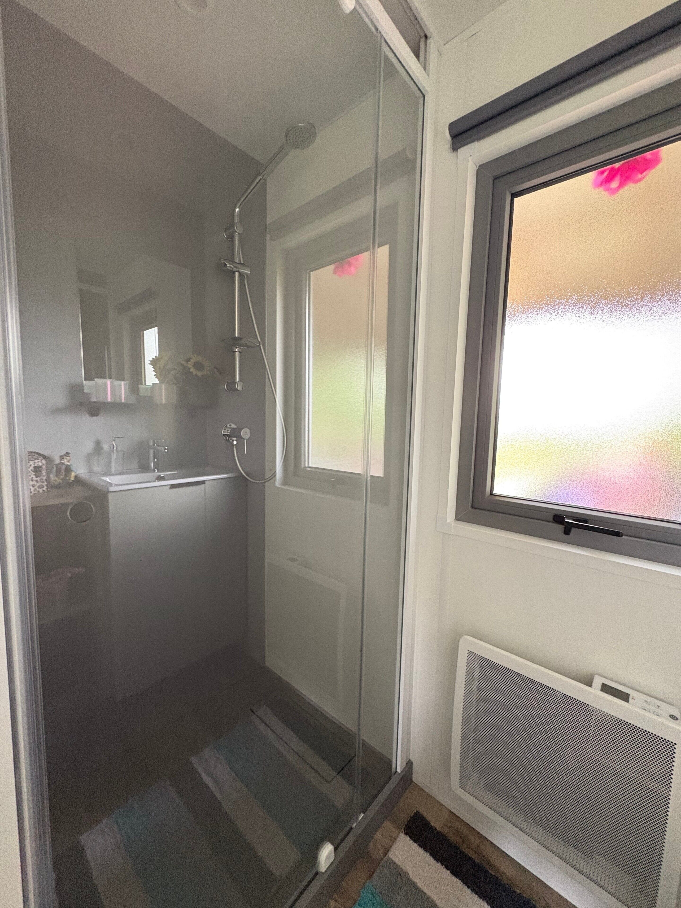Ein Badezimmer mit Duschkabine aus Glas, einem Waschbecken und einem Fenster mit Milchglas.