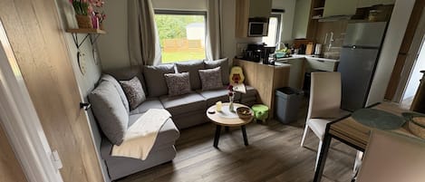 Kompakti oleskelutila, jossa on sohva, pieni ruokapöytä, keittiö ja näkymä ulos.