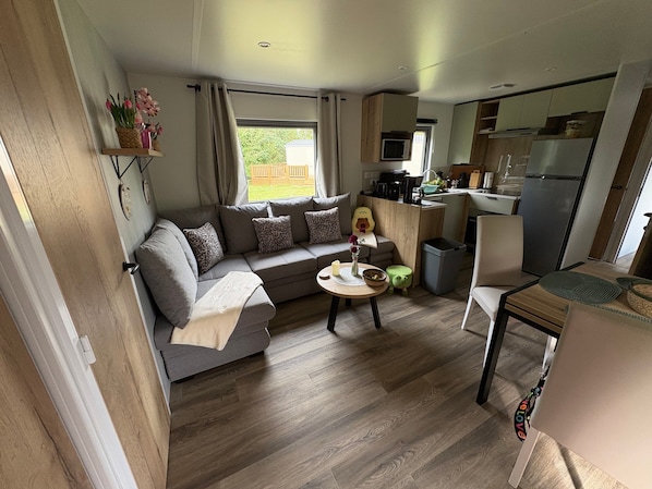 A compact living space with a sofa, a small dining table, a kitchen area, and a view of the outdoors.