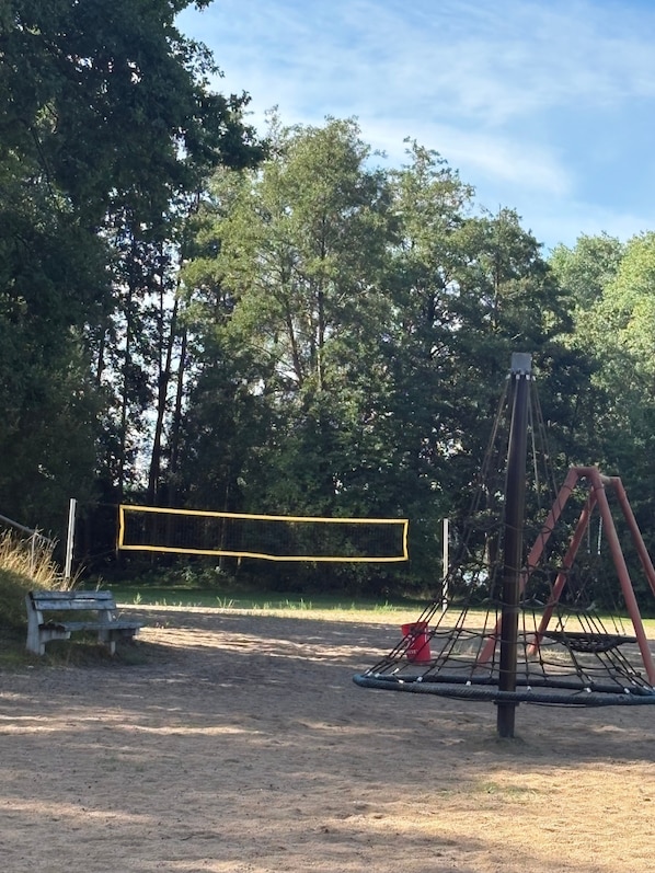 Un parque infantil con columpios y una zona amarilla cercada con red.