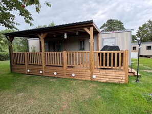 A wooden decked structure with a covered porch, a barbecue area, and a small attached building.