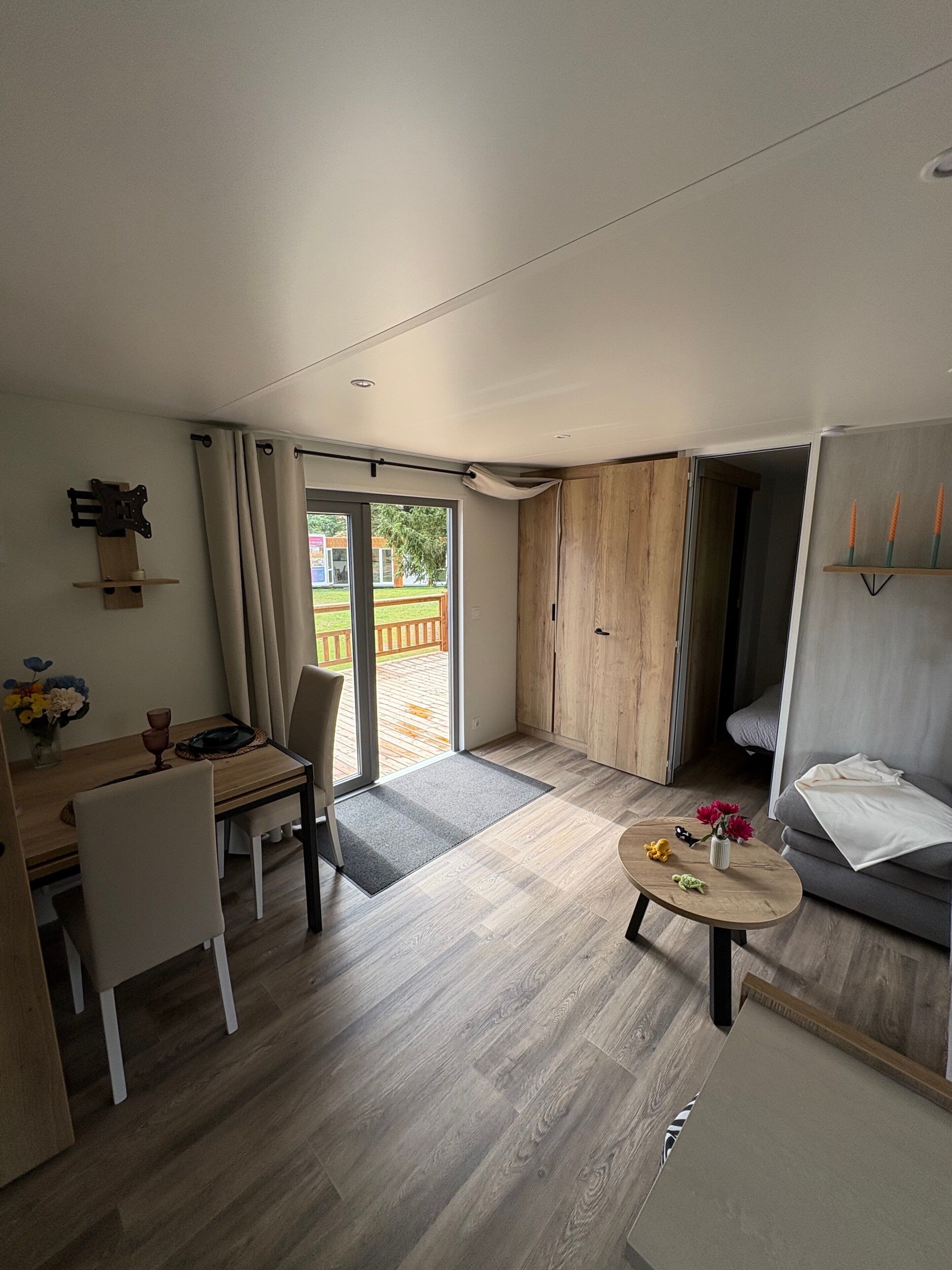 Ein modernes Wohnzimmer mit Essbereich, Holzboden, einer Couch, einem Couchtisch und Blick ins Freie.