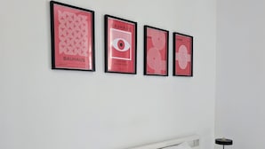 Een keurig opgemaakt slaapkamer met een wit bed, twee kussens, een nachtkastje met een lamp, en vier ingelijste posters aan de muur.