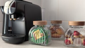 Een keukenblad met een koffiezetapparaat, een pot groene thee en twee potten ingemaakt fruit.