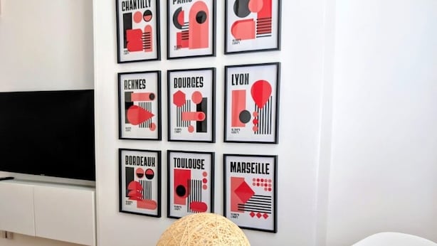 Een moderne kamer met een ronde witte tafel, een geweven bolvormig object op de tafel, en een wand met kunstwerken met stedelijke thema’s.
