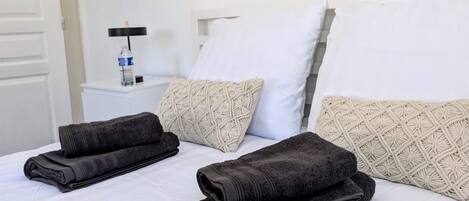 A hotel room with a bed, pillows, a nightstand with a bottle, and a door.