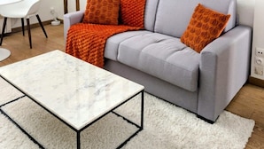 A living room with a grey sofa, orange cushions, a white coffee table, and a white rug.