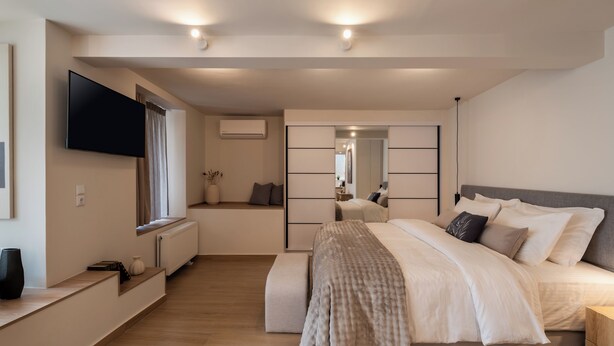 A modern bedroom with a bed, bedside tables, a TV, and a window with curtains. - Vida Zisella | Lux Home 7' from Airport (Koropi)