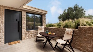 A modern outdoor seating area with a stone wall, a dark door, and a window overlooking a natural landscape. - Vida Zisella | Lux Home 7' from Airport (Koropi)