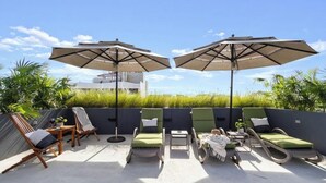 An outdoor seating area with lounge chairs and umbrellas, a concrete floor, and a view of a building in the background. - Ocean Boutique Condos (Playa del Carmen)