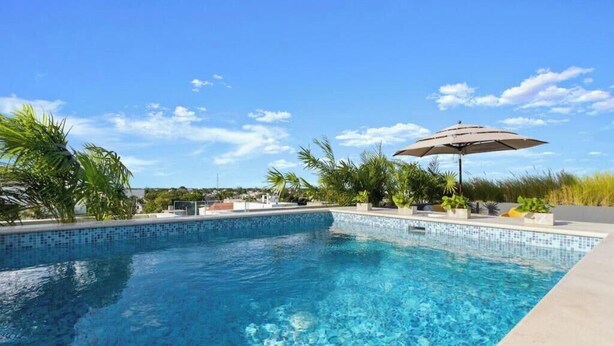 A clear blue swimming pool with a tiled edge, surrounded by greenery and a sunny sky. - Ocean Boutique Condos (Playa del Carmen)