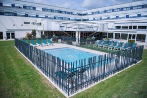 A swimming pool surrounded by a fence, with lounge chairs and a building in the background. - Ibis Budget Poitiers Site Du Futuroscope (Chasseneuil-du-Poitou)