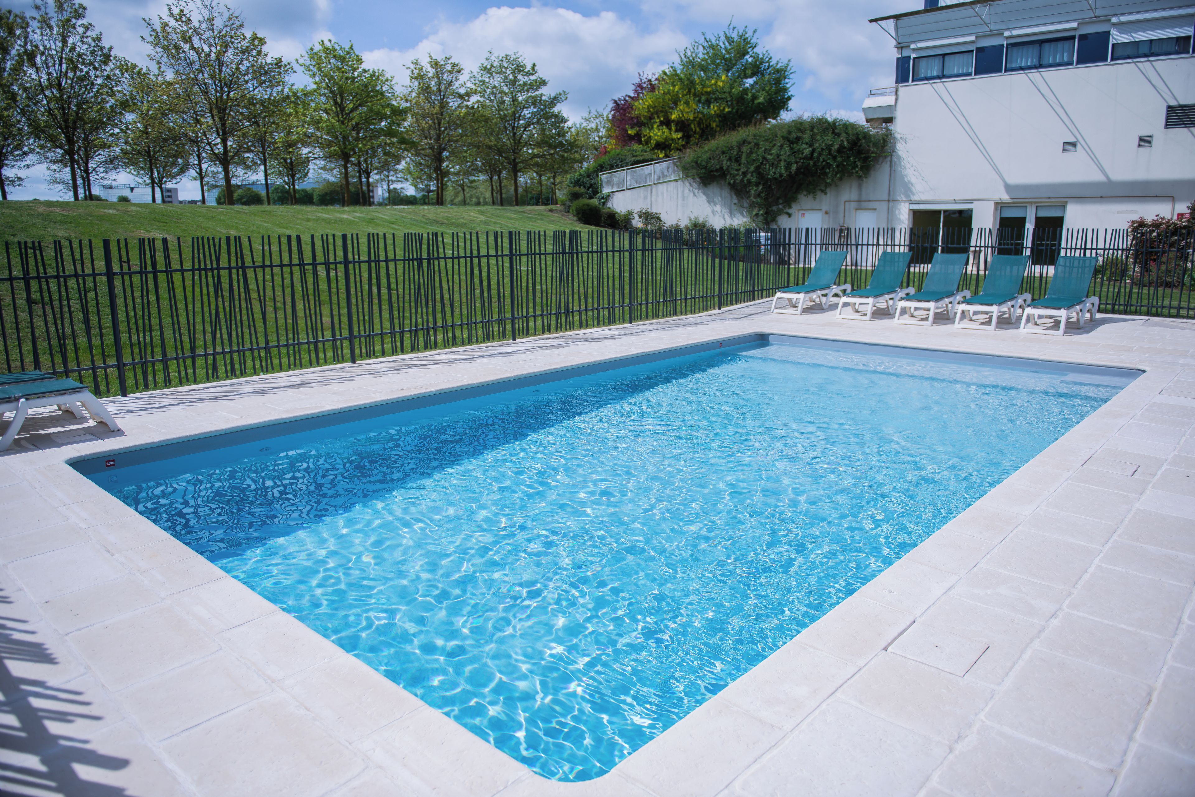 Una piscina rectangular amb aigua blava cristal·lina, envoltada per un solàrium de rajoles blanques.