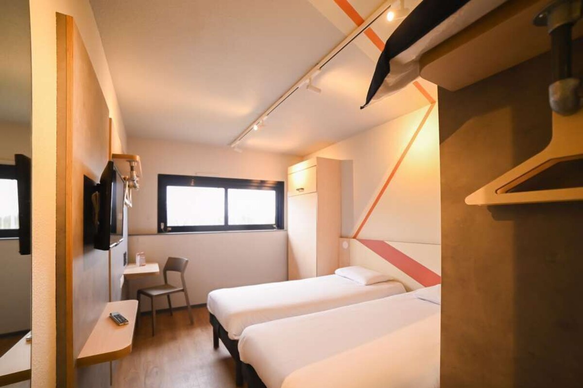A compact hotel room with two beds, a desk, and a chair.