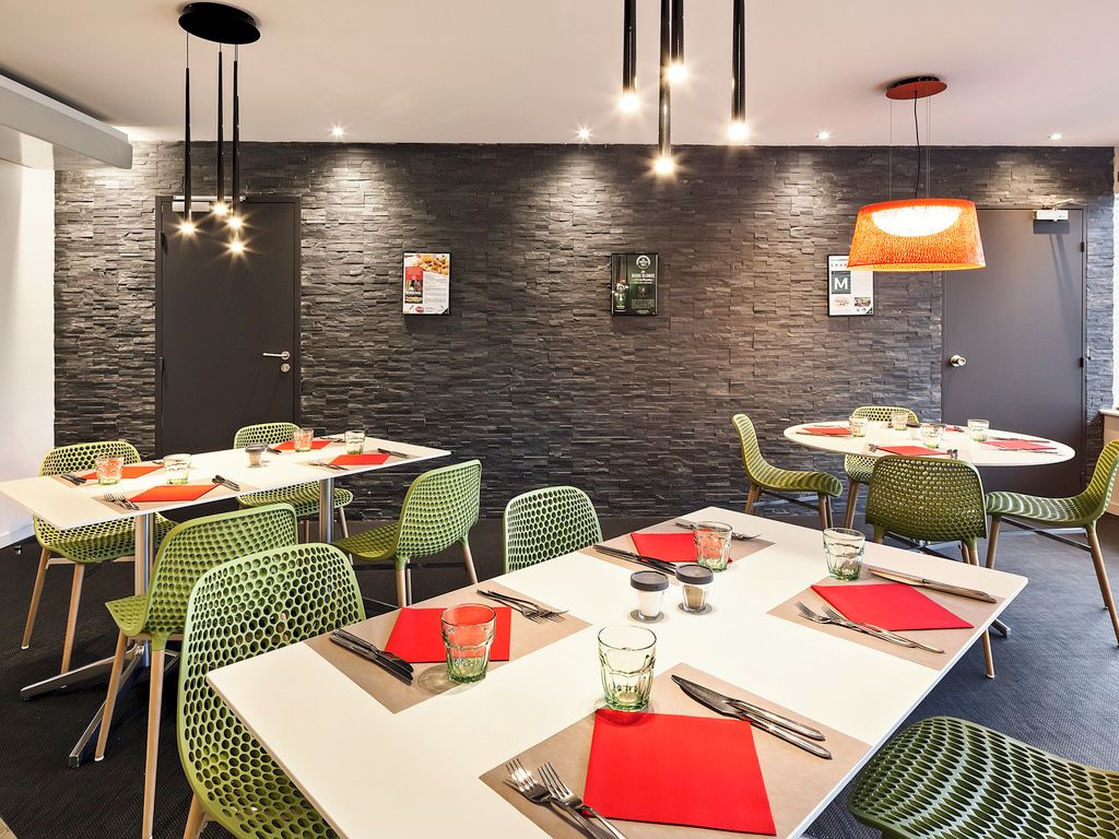 Un comedor moderno con varias mesas y sillas, una pared de piedra e iluminación colgante.