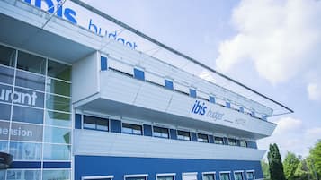 Un moderno edificio de hotel con un llamativo letrero de 'ibis budget', grandes ventanales y un techo plano.