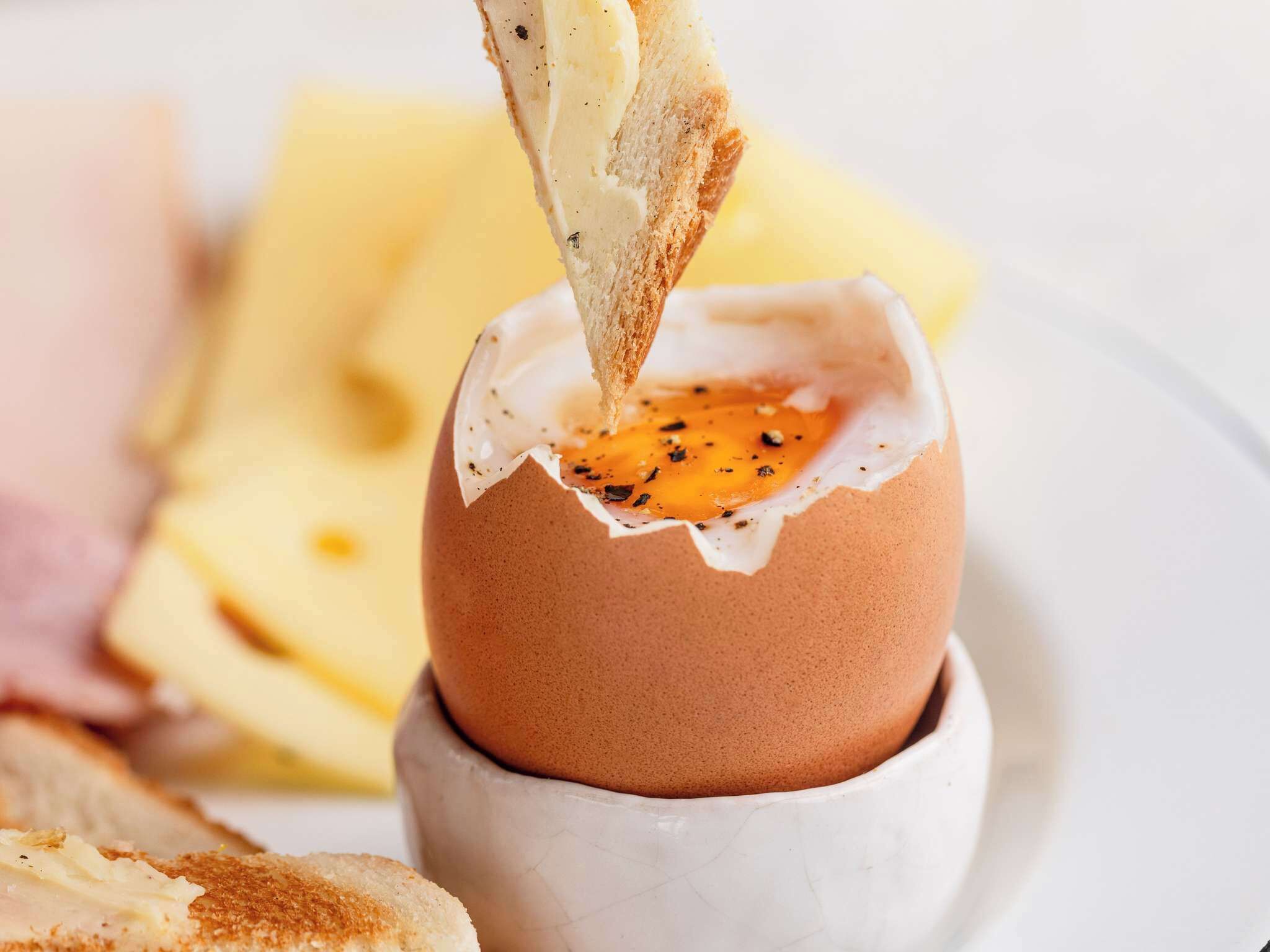 A breakfast dish with a poached egg in a cup, accompanied by toast and a side of fruit.