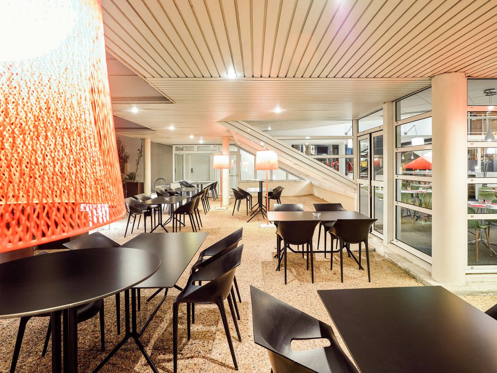 Un espace intérieur moderne, doté de tables et de chaises, d’un escalier et de grandes fenêtres.