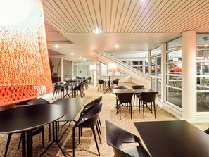 A modern indoor space with tables and chairs, a staircase, and large windows. - Ibis Budget Poitiers Site Du Futuroscope (Chasseneuil-du-Poitou)